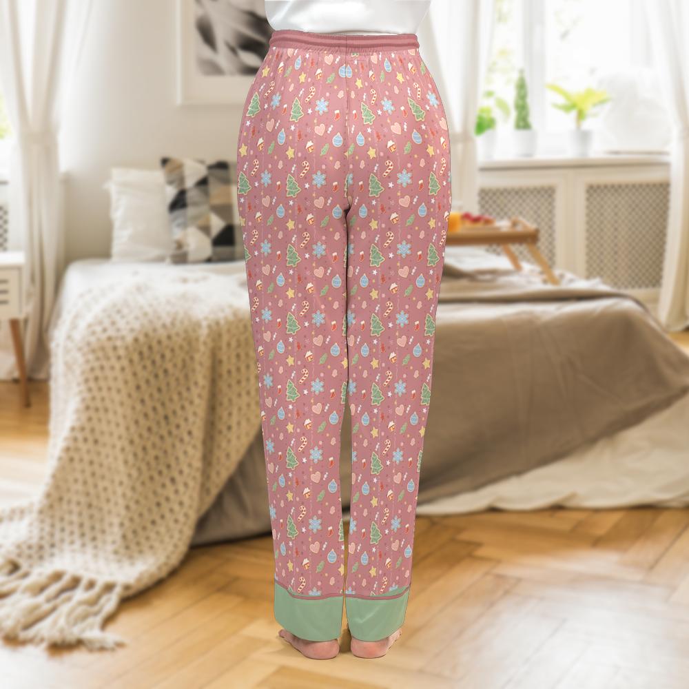 A person shown from the back wearing pink patterned pajama pants with a small multicolor print and sage green cuff trims, standing in a softly lit bedroom.