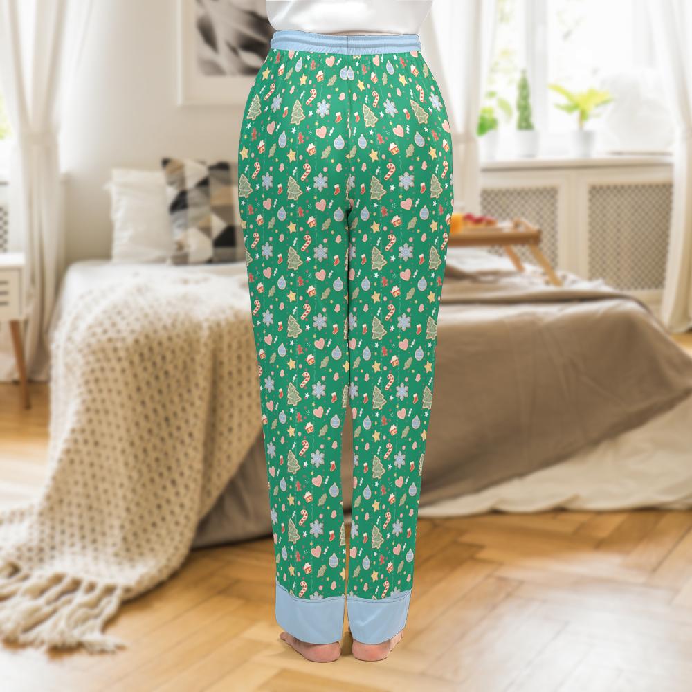 A person standing in a bedroom wearing green pajama pants with a colorful holiday tree pattern and light blue rolled cuffs, photographed from the back.