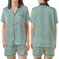 A woman modeling a two-piece pajama set shown from the front and back. The set consists of a short-sleeve button-up top and matching shorts in a light sage green color with a dense multicolor pattern of small icons, featuring dark purple trim and collar.