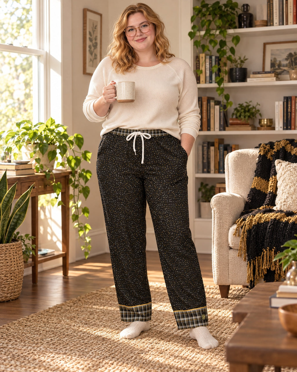 Woman in a different size standing in a cozy living room wearing the Black & Butterscotch satin pajama pants with a cream knit top