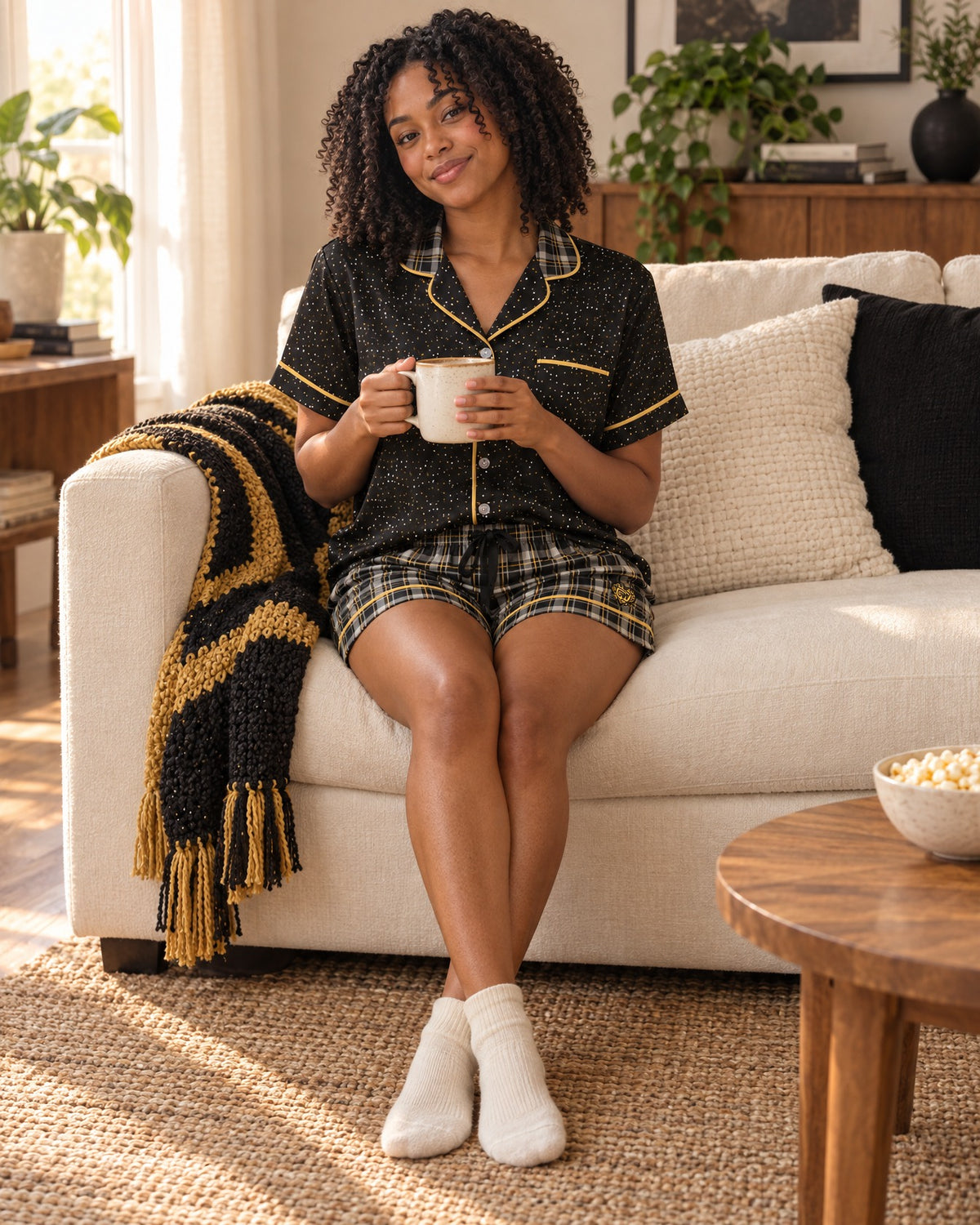 Black & Butterscotch satin pajama set worn by a woman sitting on a sofa with a coffee mug, black top with tiny white and butterscotch-gold dots