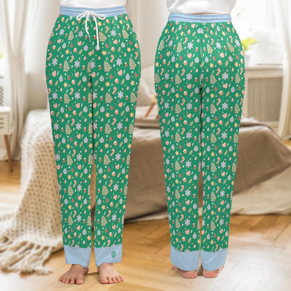 A pair of green pajama pants with a festive Christmas tree and snowflake pattern, shown from both the front and back views on a model in a bedroom setting.