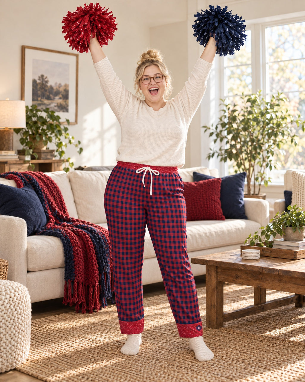 Woman cheering with both arms raised and plain pom-poms in the Cherry & Navy satin pajama pants and a cream knit top