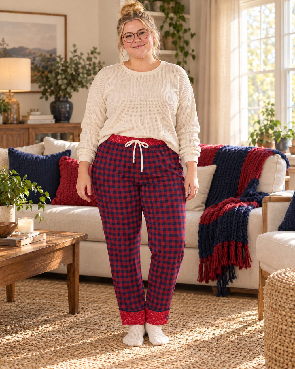 Woman standing in a sunlit living room wearing the Cherry & Navy satin pajama pants with a cream knit top