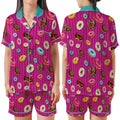 A woman modeling a two-piece pajama set shown from the front and back. The pajama set features a bright pink and purple striped background with an all-over print of colorful donuts, and has contrasting teal trim on the collar, buttons, and sleeve cuffs.