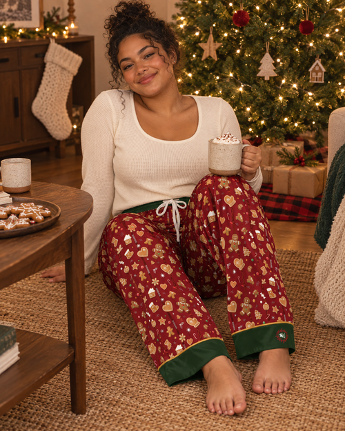 Cranberry-red satin pajama pants printed with iced gingerbread men, candy canes and snowflakes, forest-green cuffs with gold piping