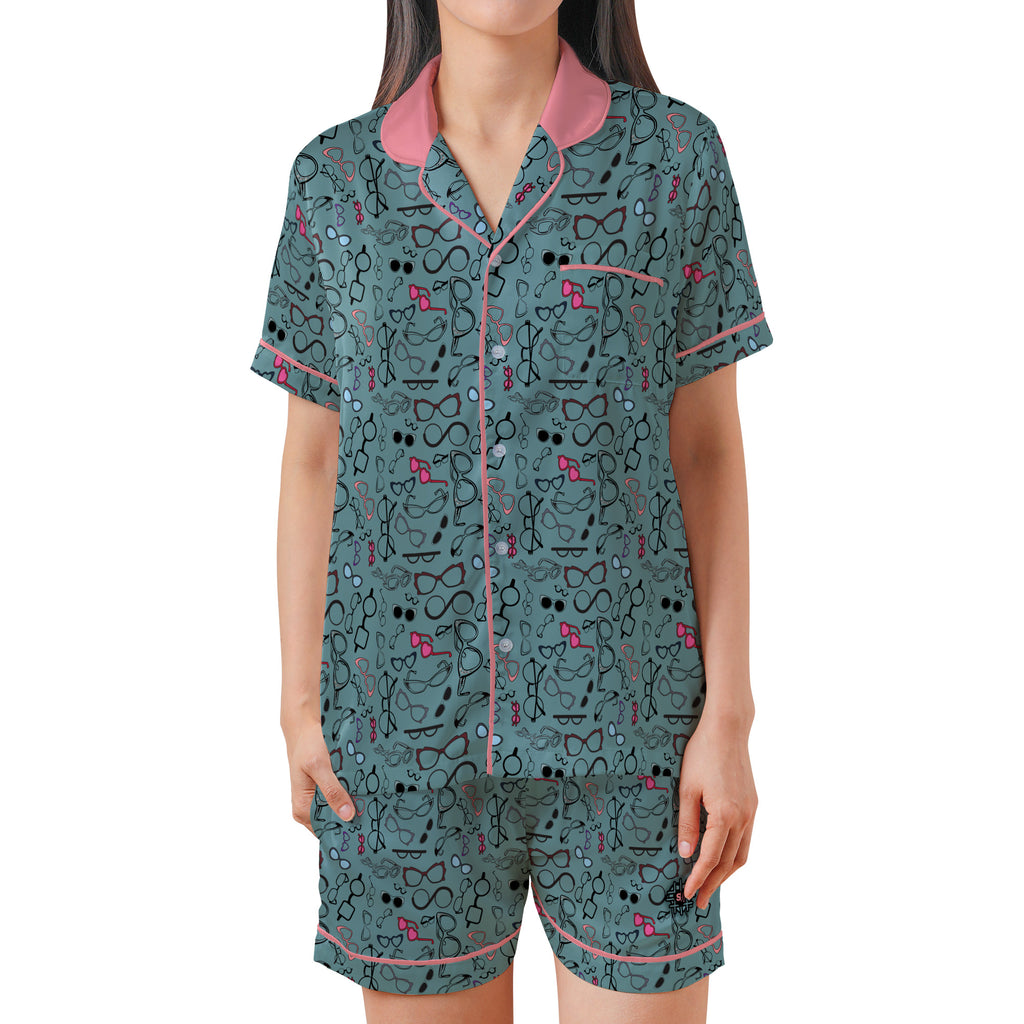 A woman modeling a matching two-piece pajama set with a teal background, black line-art pattern, and pink accents on the collar, trim, and small decorative motifs.