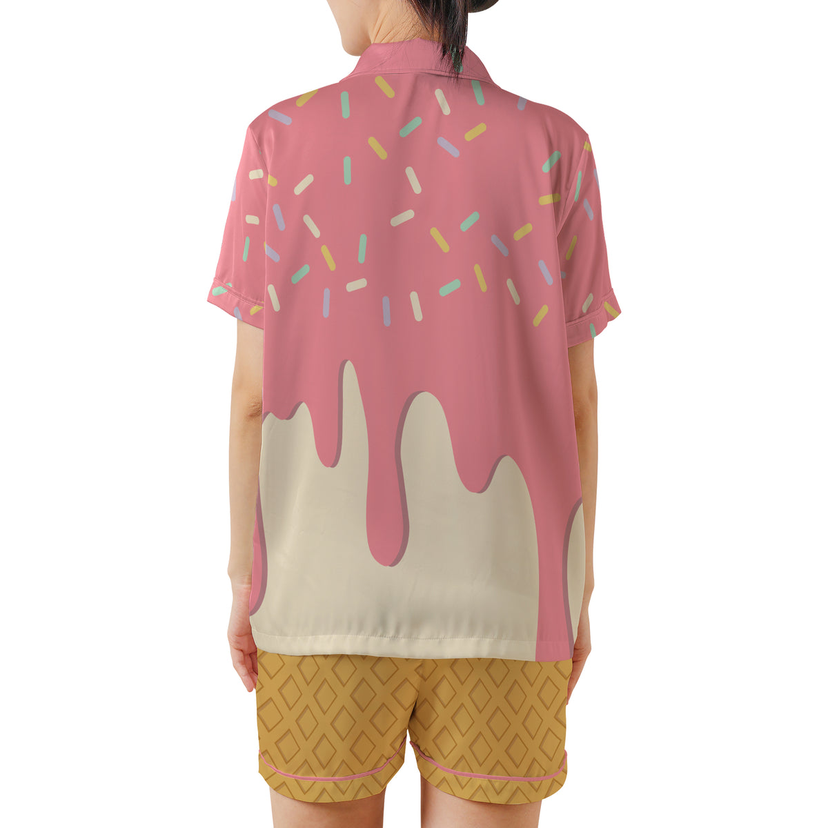 A model shown from the back wearing a short-sleeve collared shirt with a pink frosting and sprinkle print, paired with mustard yellow patterned shorts, against a plain white background.