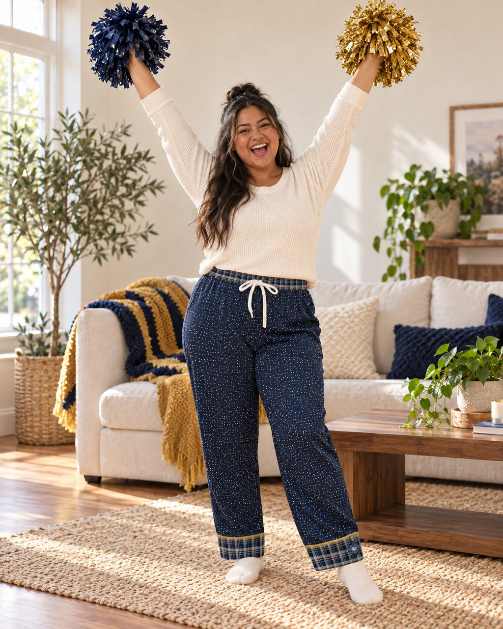 Woman cheering with both arms raised and plain pom-poms in the Navy & Brass satin pajama pants and a cream knit top
