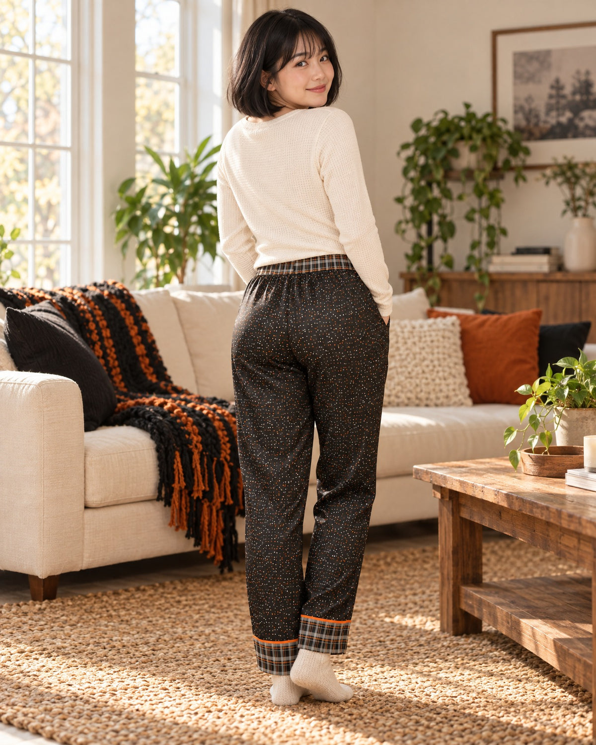 Back view of a woman in the Orange & Licorice satin pajama pants with a cream knit top, plaid waistband and cuffs