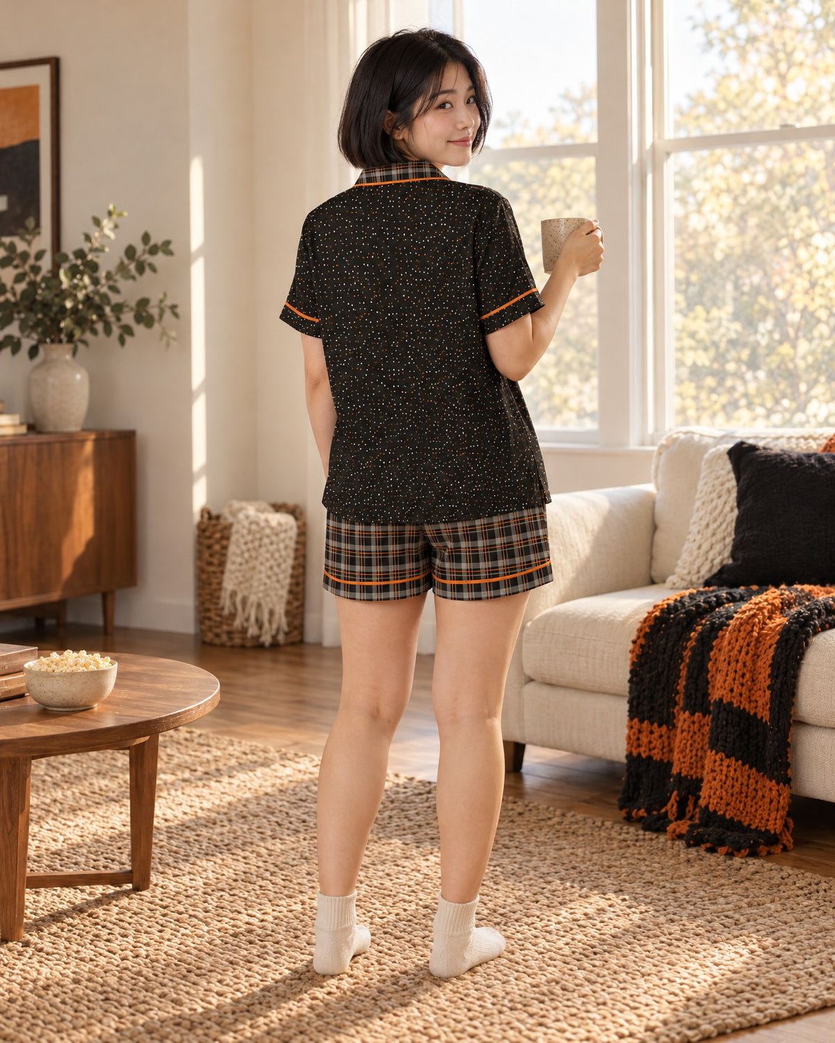 Back view of the Orange & Licorice satin pajama set, plain black top with a black and warm-gray plaid with thin orange lines collar and bright orange piping