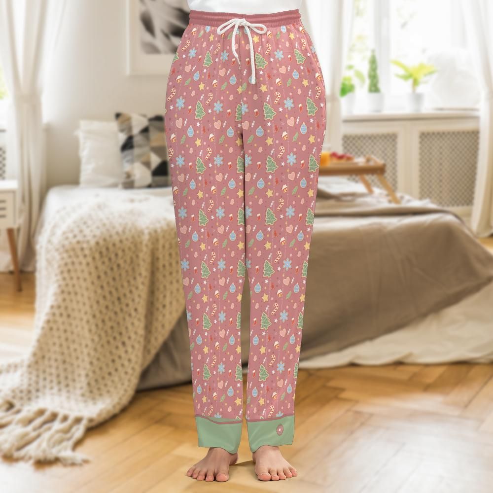 A person wearing pink patterned pajama pants with a white drawstring, shown from the waist down in a softly lit bedroom with a bed and wood floor in the background.