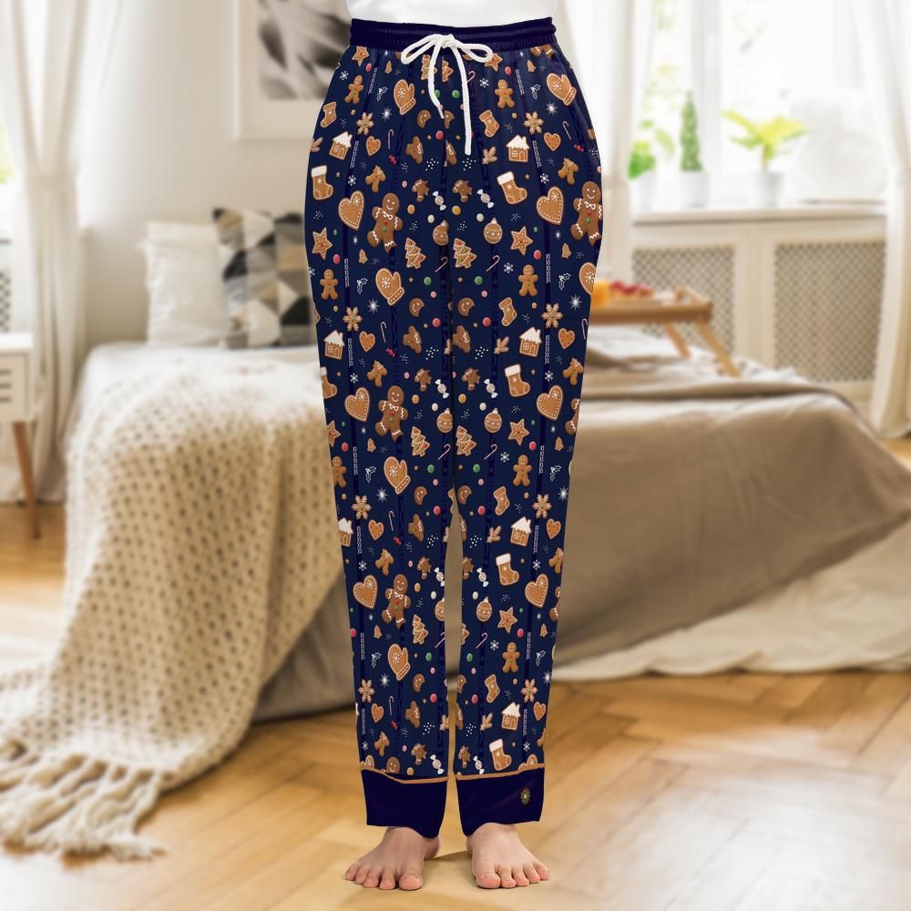 A person wearing navy blue pajama pants with a festive gingerbread-themed print, standing barefoot in a cozy bedroom setting.