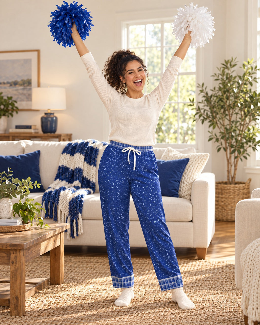Woman cheering with both arms raised and plain pom-poms in the Royal & White satin pajama pants and a cream knit top