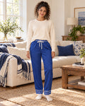 Woman standing in a sunlit living room wearing the Royal & White satin pajama pants with a cream knit top