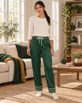 Woman standing in a sunlit living room wearing the Sage & Honey satin pajama pants with a cream knit top