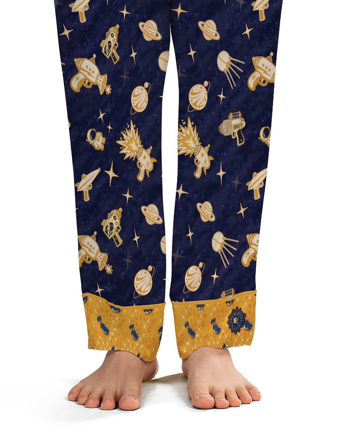 Close-up of the Space Raygun pajama pants ankle: wide mustard-gold cuff with tiny navy motifs and the Snoozewaffle waffle-grid logo badge