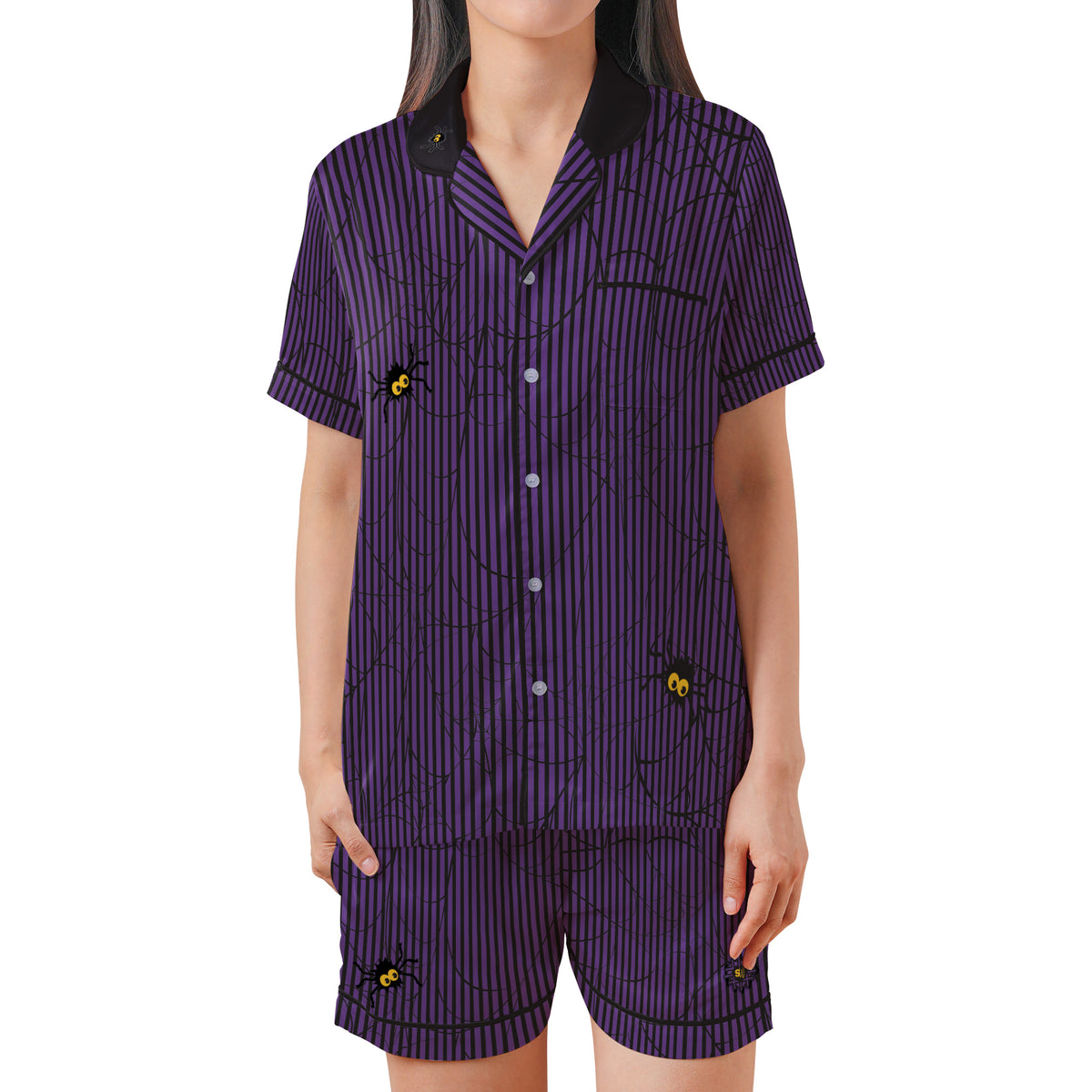 A woman modeling a matching short-sleeve button-front pajama top and shorts set in purple with thin black vertical stripes, a black spiderweb print, and small yellow-and-black spider motifs. The collar and cuffs are black.